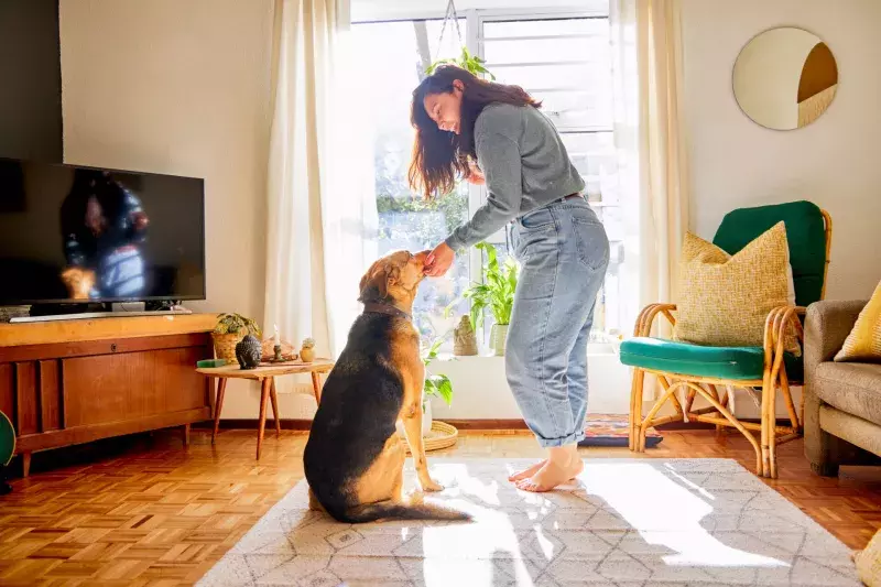 Full length shot of an attractive young woman standing alone in her living room and petting her dog