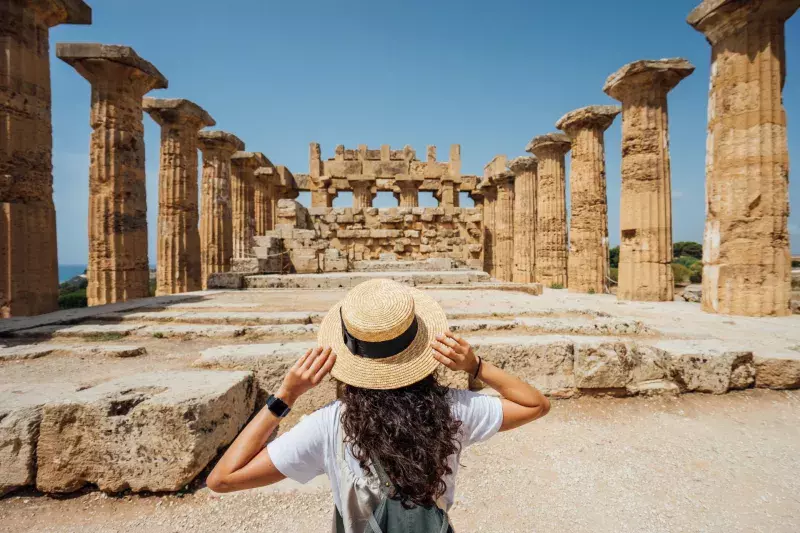 Rear view of a woman with a hat while she's admiring an ancient temple in Sicily