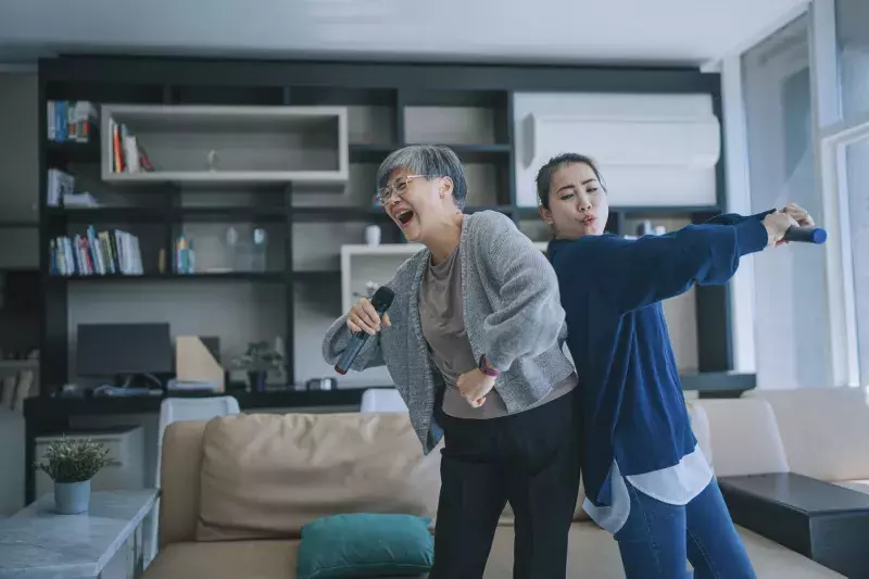 Chinese Senior woman singing karaoke dancing with her daughter in living room during weekend leisure activities