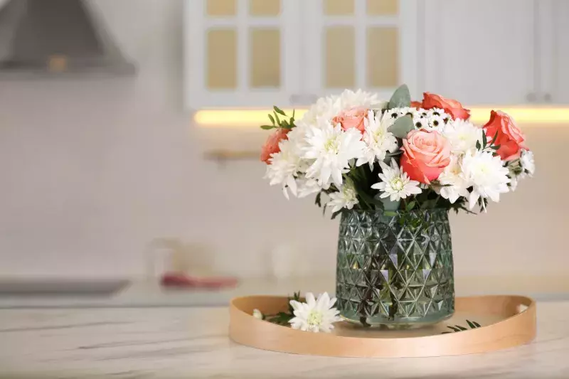 Vase with beautiful flowers on table in kitchen, space for text. Interior design