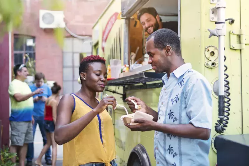 African-american couple enjoying their lunch from food truck in city street.